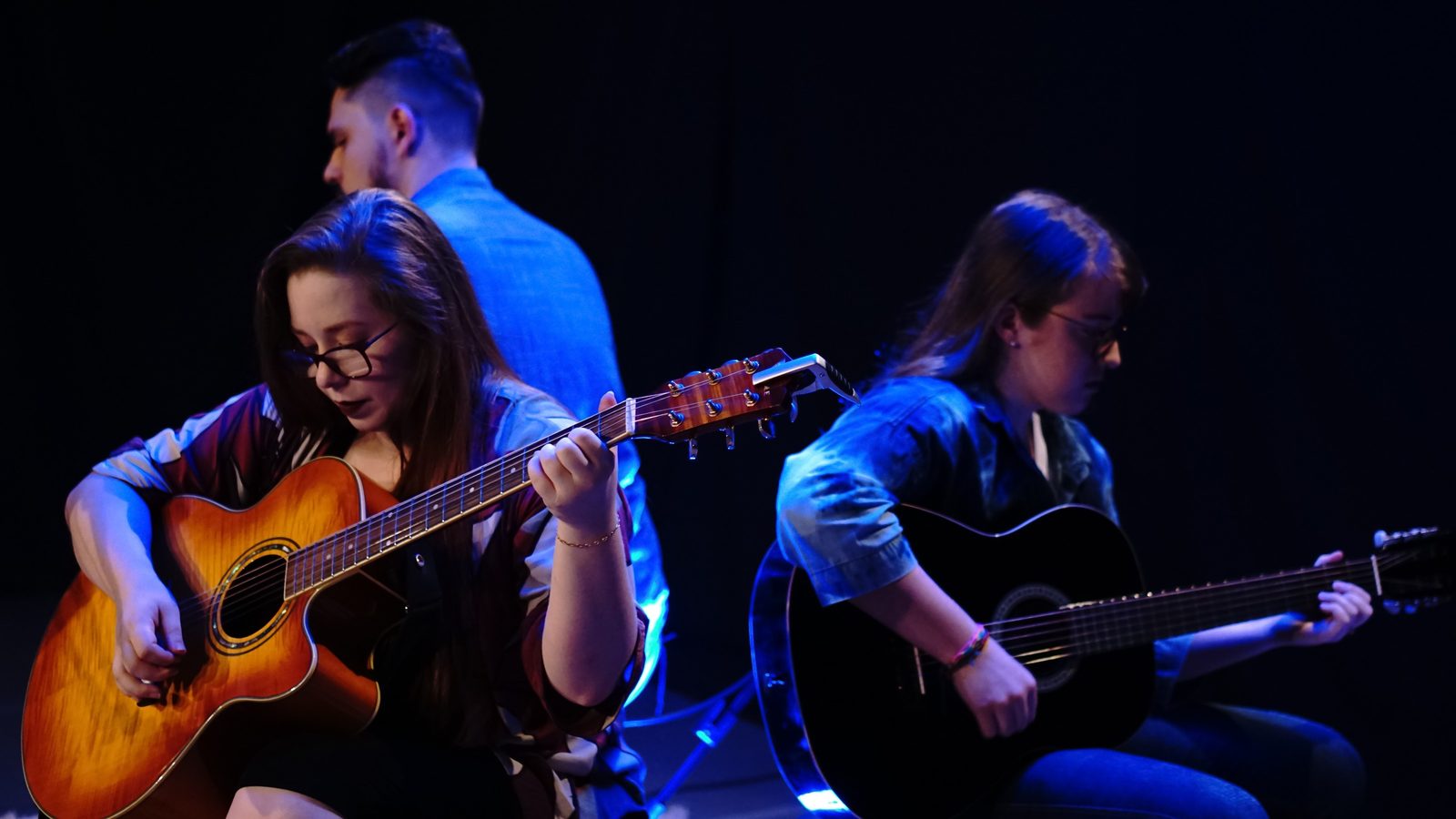 Letícia Bertoldi tocando violão ao lado de alunos no 1º Recital de Música do CAPZ